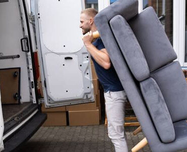 Möbellift Magdeburg: Helfer tragen ein graues Sofa aus einem Transporter
